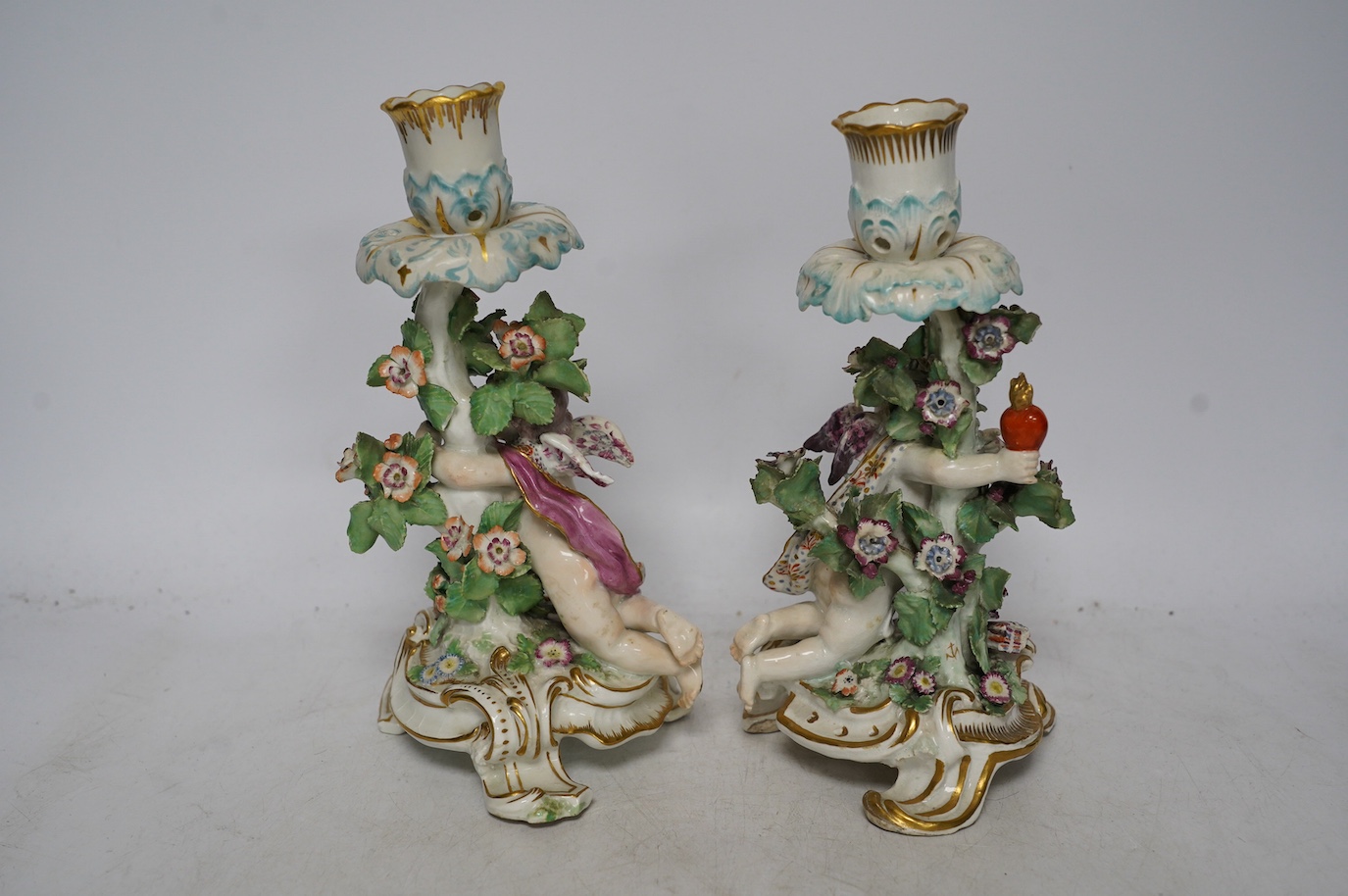 A pair of 19th century Derby porcelain candlesticks, with ‘winged cupid’ stems, 22cm. Condition - poor